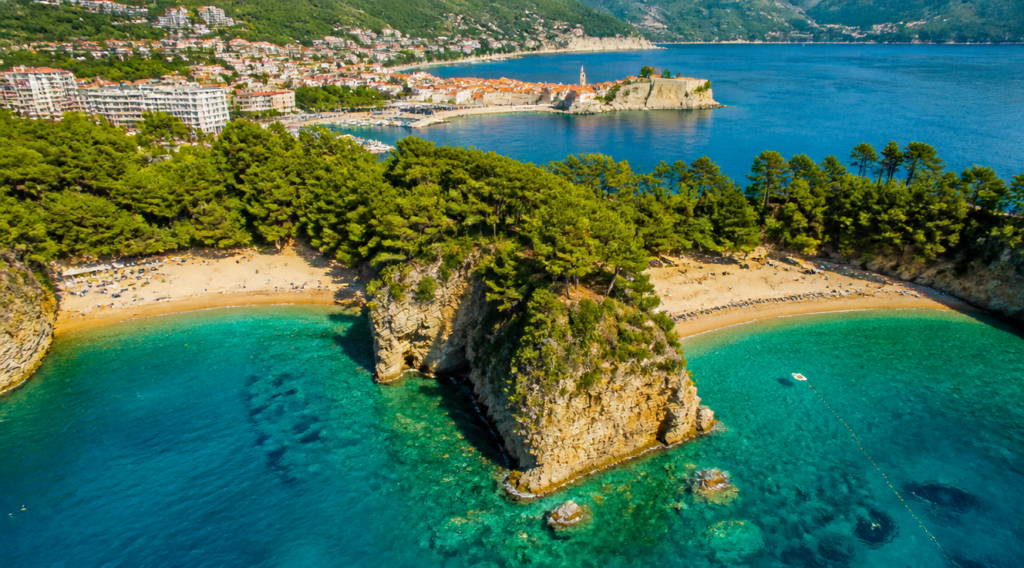 A breathtaking aerial drone photograph of Mogren Beach in Budva, Montenegro, showing two small coves separated by a dramatic rocky outcrop, crystal-clear turquoise Adriatic water, golden sandy beach, lush green pine trees on surrounding cliffs, traditional Mediterranean coastal town in the background, bright sunny day with soft golden light, photorealistic, ultra high resolution, vibrant saturated colors, summer vacation atmosphere, 4K quality